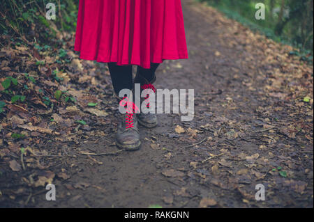 Eine Frau trägt Stiefel und ein Kleid ist zu Fuß auf einem Pfad in den Wald Stockfoto