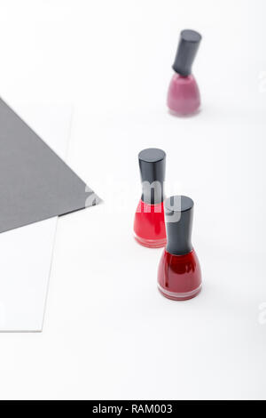 Blick von oben auf die drei Flaschen Rot, Burgund und rosa Nagellack auf Weiß Stockfoto