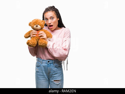 Junge afrikanische American Girl holding Teddybär über isolierte Hintergrund im Schlag mit einer Überraschung konfrontiert, ängstlich und aufgeregt mit Angst Angst Ausdruck Stockfoto