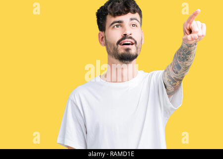 Jungen gutaussehenden Mann tragen weiße T-Shirt über isolierte Hintergrund zeigt mit Finger vor überrascht, offenem Mund erstaunt Ausdruck, etwas in her Stockfoto