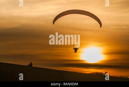 Firle, Lewes, East Sussex, Großbritannien. Januar 2019. Gleitschirmfliegen in der Nördlichen Brise, während die Sonne über die South Downs hinuntergeht. Stockfoto