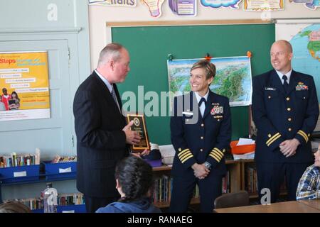 Thomas Matthews, Principal von Trowbridge Schule der Entdeckung und Technologie im Bay View, Wis., nimmt eine Plakette der Wertschätzung von Kapitän Amy Cocanour, der Kommandant der Küstenwache Sektor Michigan See in Milwaukee, und Leutnant Jesse Webster, Leiter der Reserve Bereitschaft Kräfte für den Sektor Lake Michigan, in Anerkennung der Partnerschaft in Bildung zwischen den beiden Organisationen Feb 21, 2017. Coast Guard Sektor Lake Michigan wurde mit der "besten Einheit Partnerschaft" in der Küstenwache für die mehr als 900 freiwilligen Stunden durch seine Mitglieder, die Studenten in Bradford-on-Avon Schule der Entdeckung und Te zur Verfügung benannt Stockfoto