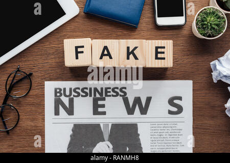 Blick von oben auf die holzwürfel mit Word fake und Wirtschaftszeitung auf hölzernen Tischplatte Stockfoto