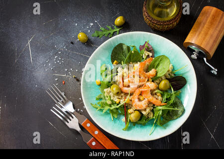 Diätmenü, veganes Essen. Gesunde Salate mit Quinoa, Rucola, Garnelen und Oliven auf einem dunklen Stein Tabelle. Stockfoto