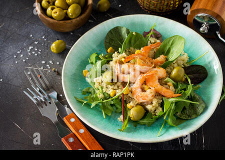 Diätmenü, veganes Essen. Gesunde Salate mit Quinoa, Rucola, Garnelen und Oliven auf einem dunklen Stein Tabelle. Stockfoto