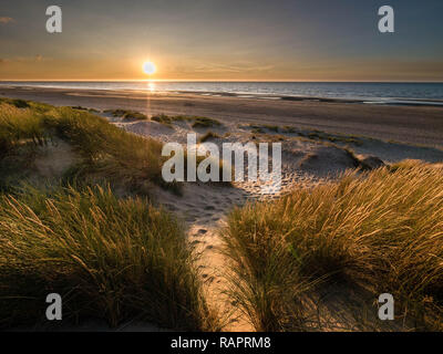 Blick vom bunten marram Gras bedeckte Dünen im Norden Frankreichs in Richtung der Sonne bereit, in den Ozean zu verschwinden Stockfoto