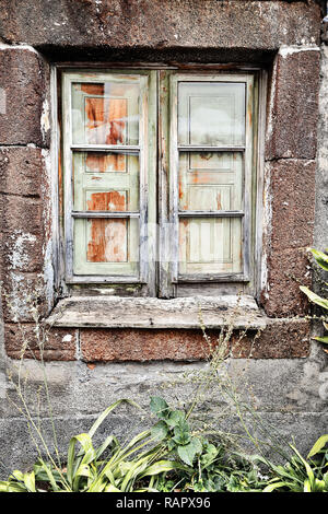 Eine marode Holzfenster in einem alten Haus aus Stein auf Madeira, Portugal. Das Fenster von innen durch die Fensterläden geschlossen ist, werden die Frames sind unlackiert und Stockfoto