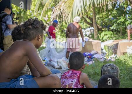 Insel Kinder warten und beobachten, während ihre dorfchefs sortieren und verteilen Hilfsgüter für gleiche Verteilung im Betrieb Weihnachten Drop, 10.12.2018, Auf Fais Island, Föderierte Staaten von Mikronesien. Obwohl Fais hat eine kleine Landebahn, die Inselbewohner erhalten selten Besucher, Mail, oder Lieferungen und OCD jedes Jahr Look für den Nachschub von Kleidung, Angeln, pädagogische und medizinische Versorgung. Stockfoto