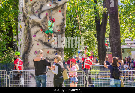 Der kleine Junge in einem Kabelbaum klettern eine Wand mit Grips im Freien Stockfoto