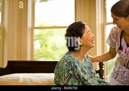 Weibliche Krankenschwester lächelt und setzt eine beruhigende Hand auf die Schulter eines älteren Frau. Stockfoto