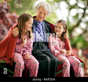 Lächelnde ältere Frau sitzt mit ihren beiden Enkelinnen. Stockfoto