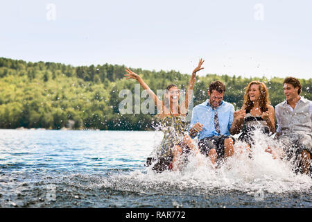 Gruppe von Freunden sitzen auf einem Steg, Planschen im See mit ihren Beinen. Stockfoto