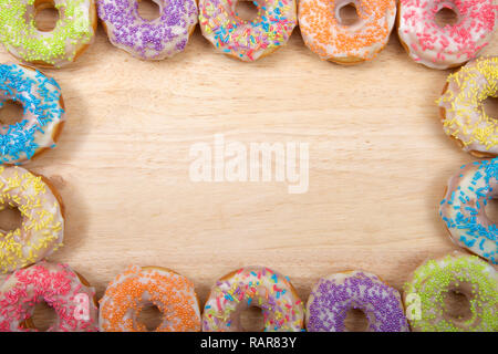 Flach Ansicht vieler Frosted Donuts mit Süßigkeiten besprüht in einem grenzüberschreitenden Rahmen auf hellem Holz Tisch mit Kopie Raum angeordnet. Stockfoto