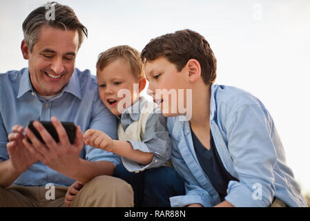 Reifer Mann sein Handy zu zeigen seine neugierigen Kinder. Stockfoto