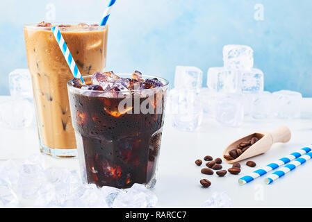 Sommer trinken Eiskaffee in einem Glas Kaffee mit Sahne und Eis in ein hohes Glas, Kaffeebohnen und Strohhalme durch Eis auf weißem Marmor Tabelle über bl umgeben Stockfoto