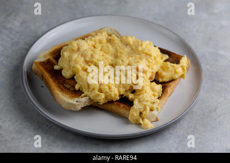 Rührei auf zwei Scheiben Toast auf eine weiße Platte mit einem grauen Rand auf einer einfachen Grau und Weiß marmorierten Hintergrund Stockfoto