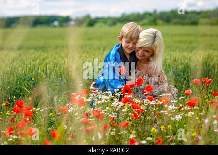 Mutter mit ihrem Sohn in einer herrlichen Wiese. Der junge überrascht ihre Mutter mit roter Mohn. Stockfoto