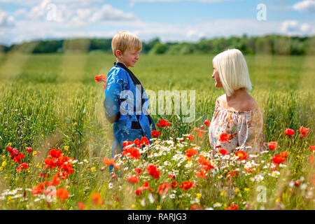 Mutter mit ihrem Sohn in einer herrlichen Wiese. Der junge überrascht ihre Mutter mit roter Mohn. Stockfoto