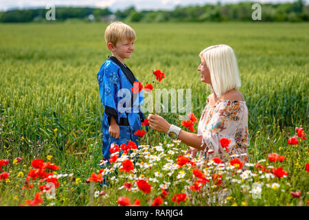 Mutter mit ihrem Sohn in einer herrlichen Wiese. Der junge überrascht ihre Mutter mit roter Mohn. Stockfoto