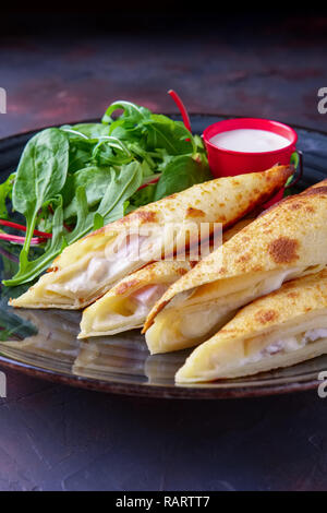 Dünne Pfannkuchen mit Schinken und Käse mit Spinat, Rucola, Mais und Mangold Salat serviert. Stockfoto