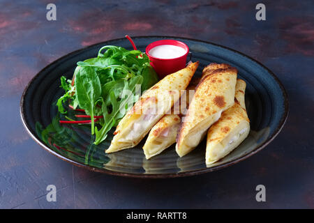 Dünne Pfannkuchen mit Schinken und Käse mit Spinat, Rucola, Mais und Mangold Salat serviert. Stockfoto