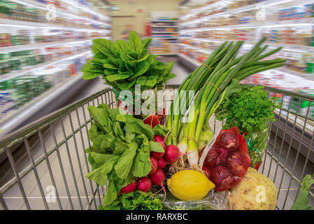 Einkaufswagen mit Gemüse, das durch einen Supermarkt fährt Stockfoto