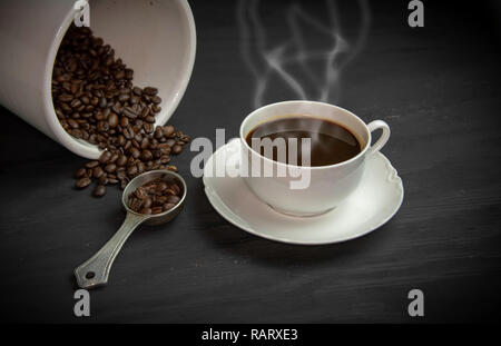 Dampfende Tasse Kaffee in weißes Porzellan Tasse und Untertasse mit Kaffeebohnen in Container. Stockfoto