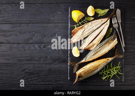 Heiß geräucherte Makrele, serviert auf einem schwarzem Schiefer Fach mit Salz, Pfeffer, Rosmarin und Zitronenscheiben, Messer und Gabel, von oben betrachten, flatlay, Kopieren spac Stockfoto