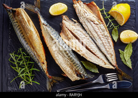 Nahaufnahme der geräucherte Makrele, serviert auf einem schwarzem Schiefer Fach mit Salz, Pfeffer, Rosmarin und Zitronenscheiben, Messer und Gabel, Ansicht von oben, flatlay Stockfoto