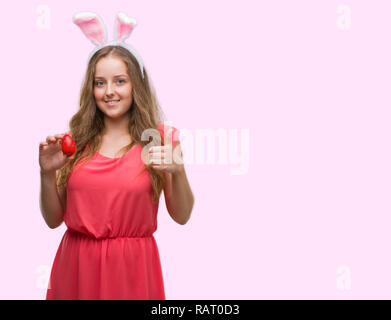 Junge blonde Frau bekleidet Osterhasen Ohren mit Lächeln tun ok Zeichen glücklich, Daumen hoch, mit den Fingern, ausgezeichnete Zeichen Stockfoto