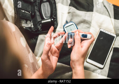 Thema Diabetes. Eine Nahaufnahme Makro planen. Die Hände eines jungen kaukasischen Frau zu Hause im Schlafzimmer auf dem Bett. Es nutzt die Technologie eines Instruments für Stockfoto