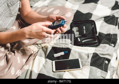 Thema Diabetes. Eine Nahaufnahme Makro planen. Die Hände eines jungen kaukasischen Frau zu Hause im Schlafzimmer auf dem Bett. Es nutzt die Technologie eines Instruments für Stockfoto