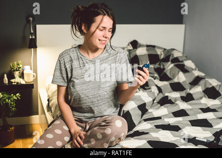 Thema Diabetes. jungen kaukasischen Frau zu Hause im Schlafzimmer auf dem Bett die Technologie der verwendet das Gerät für die Messung von Blutzucker, glucometer Test Stockfoto