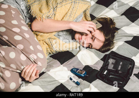 Thema Diabetes. junge Frau home Schlafzimmer Bett verwendet die Technologie gerät Messung der Blutzuckerwerte, glucometer Teststreifen hohe Blutzuckerspiegel Krankheit. C Stockfoto