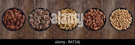 Close-up von oben der gesunden Pekannüsse, Walnüsse, Cashewnüsse, Mandeln, Erdnüsse in eine Schüssel geben. Nahaufnahme von verschiedenen Muttern auf ein Holzbrett. Mischung aus gesunden Nu Stockfoto