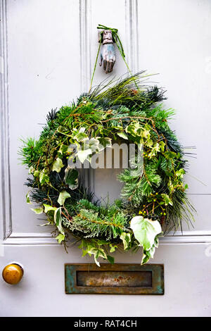 Weihnachten Kranz in Ivy und Tanne hängen auf einer traditionellen Holz Tür mit Messing Briefkasten und hand Klopfer in Port Isaac gemalt Stockfoto