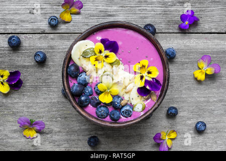 Gesundes Frühstück smoothie Schüssel garniert mit frischen Beeren, Banane, Chia Samen und Blumen. top View Stockfoto