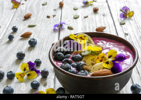 Smoothie Schüssel garniert mit frischen Beeren, Banane, Chia Samen, Nüsse und Blumen für eine gesunde vegetarische Ernährung Frühstück. Nach oben Schließen Stockfoto