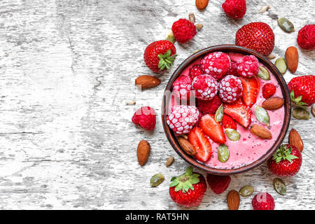 Smoothie Schale mit roten Beeren - Erdbeeren und gefrorene Himbeeren, Nüsse und Samen für eine gesunde vegetarische Ernährung Frühstück. Ansicht von oben mit der Kopie Raum Stockfoto