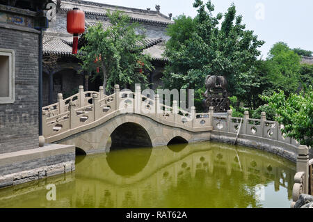 Brücke über einen Teich in einem Innenhof mit Bäumen und Fische Skulptur in Pingyao, Shanxi, China Stockfoto