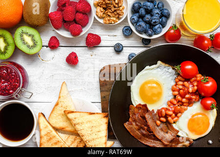 Englisches Frühstück - Spiegeleier, Bohnen, Tomaten, Kaffee, Speck und Toast mit frischen Früchten und Beeren. Ansicht von oben Stockfoto