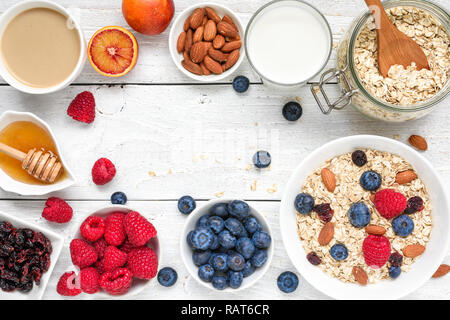 Essen Rahmen aus Frühstück Zutat. Müsli, Früchte, Beeren, Cappuccino, nony, Milch und Muttern auf weiße Holztisch. gesundes Essen. Ansicht von oben mit c Stockfoto