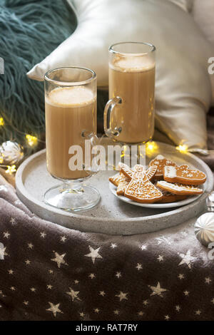 Hausgemachte Latte in Glas Tassen, serviert mit Lebkuchen auf dem Hintergrund der Plaid, Kissen und Girlanden. Stockfoto