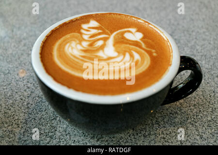 Heißen Cappuccino mit schönen Latte Art in einem schwarzen Schale serviert auf grauem Stein Tabelle Stockfoto