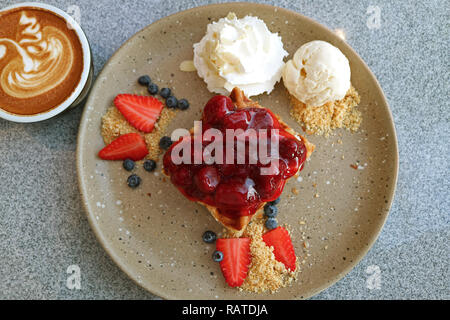 Blick von oben auf die Waffel mit erdbeersauce, frische Beeren, Vanille Eis und einer Tasse heißen Kaffee cuppuccino Stockfoto