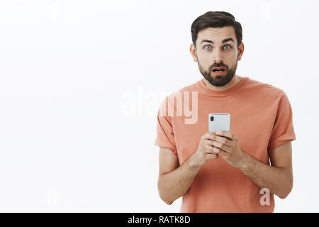 Taille-up Shot von überrascht und schockiert stattlichen kaukasischen Typ mit Bart offenen Mund clueless Holding smartphone quesitoned nach Erhalt verwirrende Sms über grauer Hintergrund wird betäubt Stockfoto