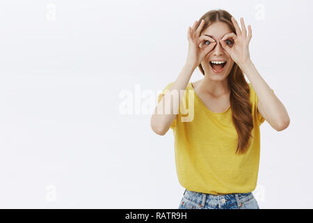 Taille-up Shot lustige aufgeregt und kreative Happy kaukasische Mädchen mit Zopf in gelben T-Shirt Kreise über die Augen, als wenn Sie durch Schutzbrille erstaunt lächelnd Gefühl überrascht und begeistert Stockfoto