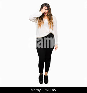 Junge schöne Frau tragen weiße Pullover peeking im Schock für Gesicht und Augen mit der Hand, schauen durch die Finger mit peinlich Ausdruck. Stockfoto