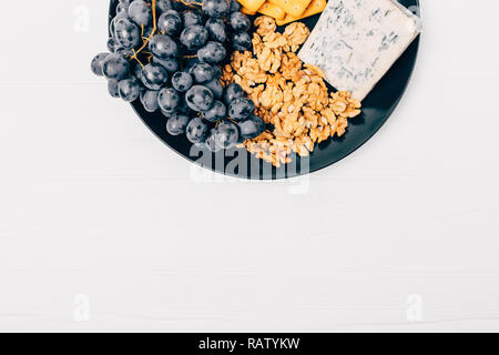 Ansicht von oben Platte mit Käse, Trauben, Cracker und Walnüsse auf weissem Holztisch. Stockfoto