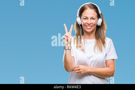 Mittleres Alter Hispanic Frau Musikhören mit Kopfhörern über isolierte Hintergrund lächelnd mit glücklichen Gesicht in die Kamera tun Sieg winking s Stockfoto
